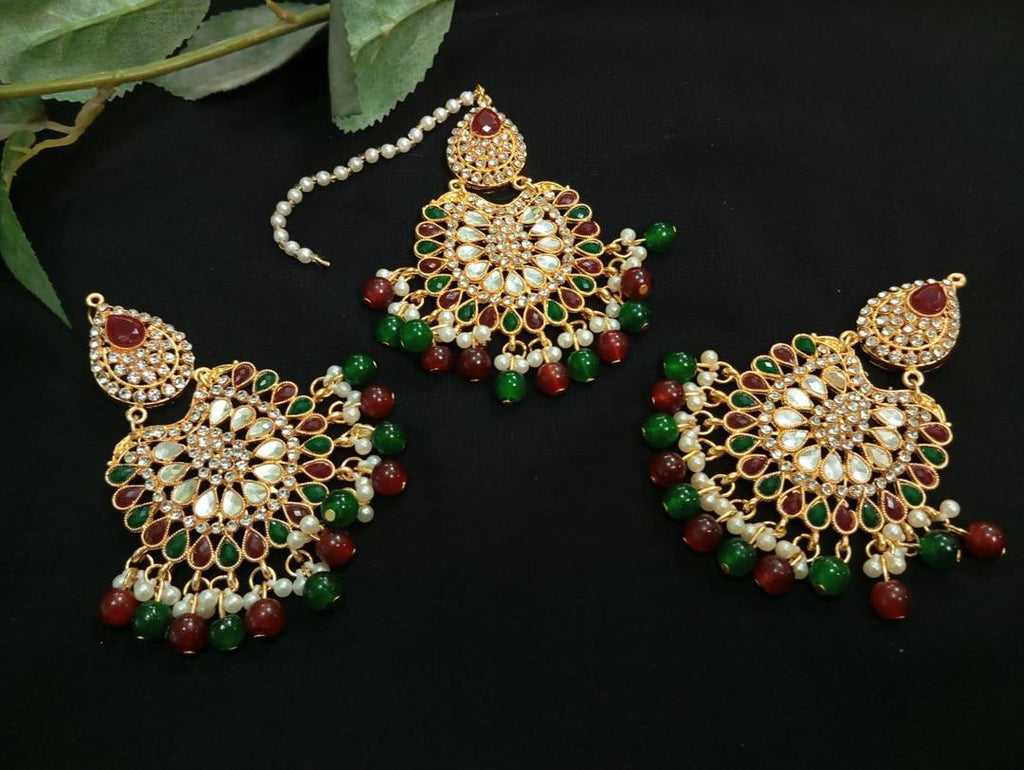 Ornate gold jewelry set with red and green stones on a dark background
