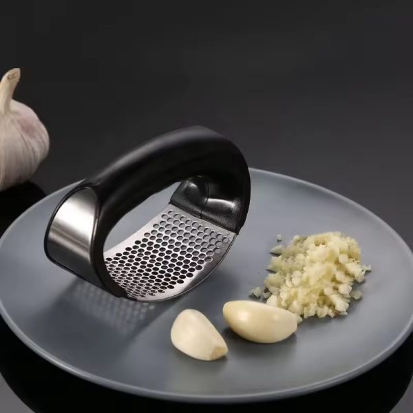 Garlic press with crushed garlic on a gray plate against a black background