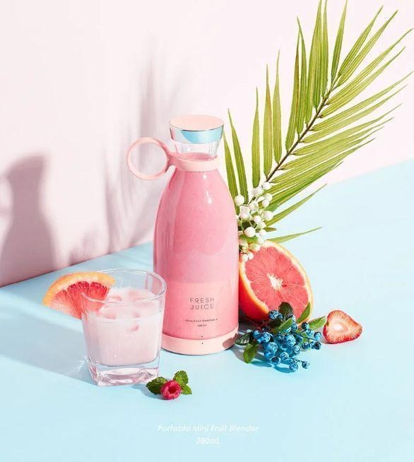 Pink thermos bottle with a glass of pink drink and grapefruit on a light blue background