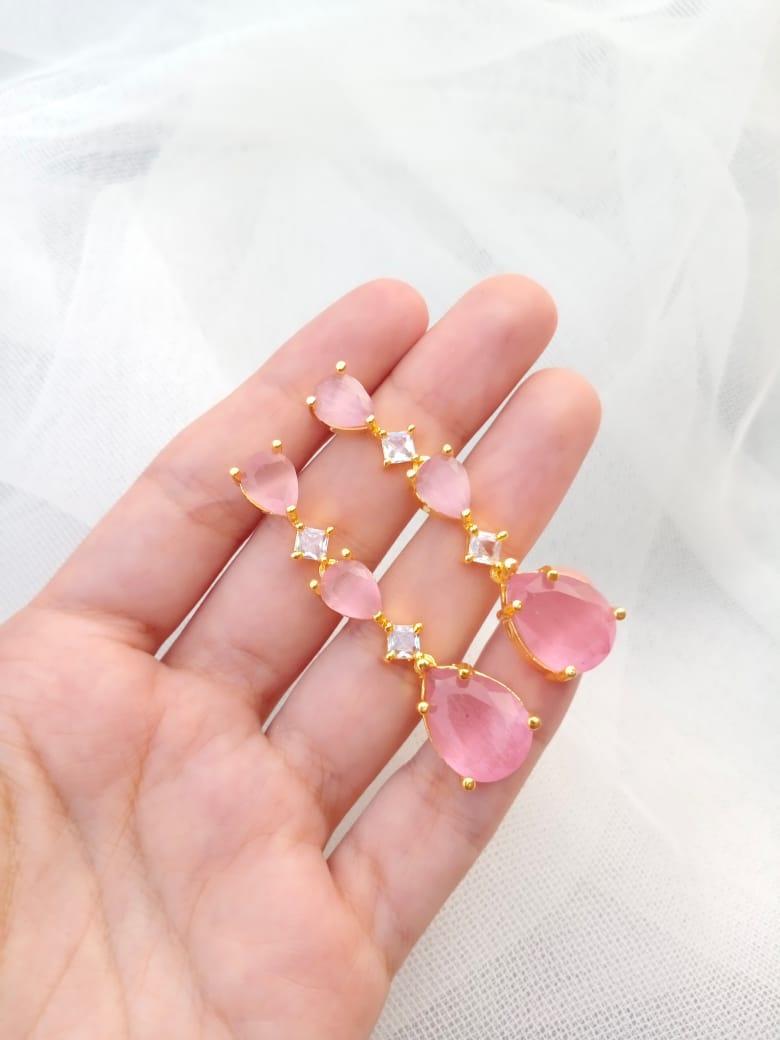 Pink teardrop earrings with gold accents held in a hand against a white background