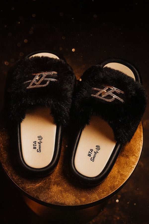 Black fuzzy slippers with brand logo on a dark background