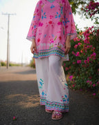 Person wearing a pink floral top and white pants with floral patterns, standing outdoors.