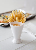 White ceramic cup filled with French fries on a light wooden surface