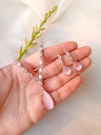 Hand holding a pair of pink teardrop earrings with clear stones on a light background