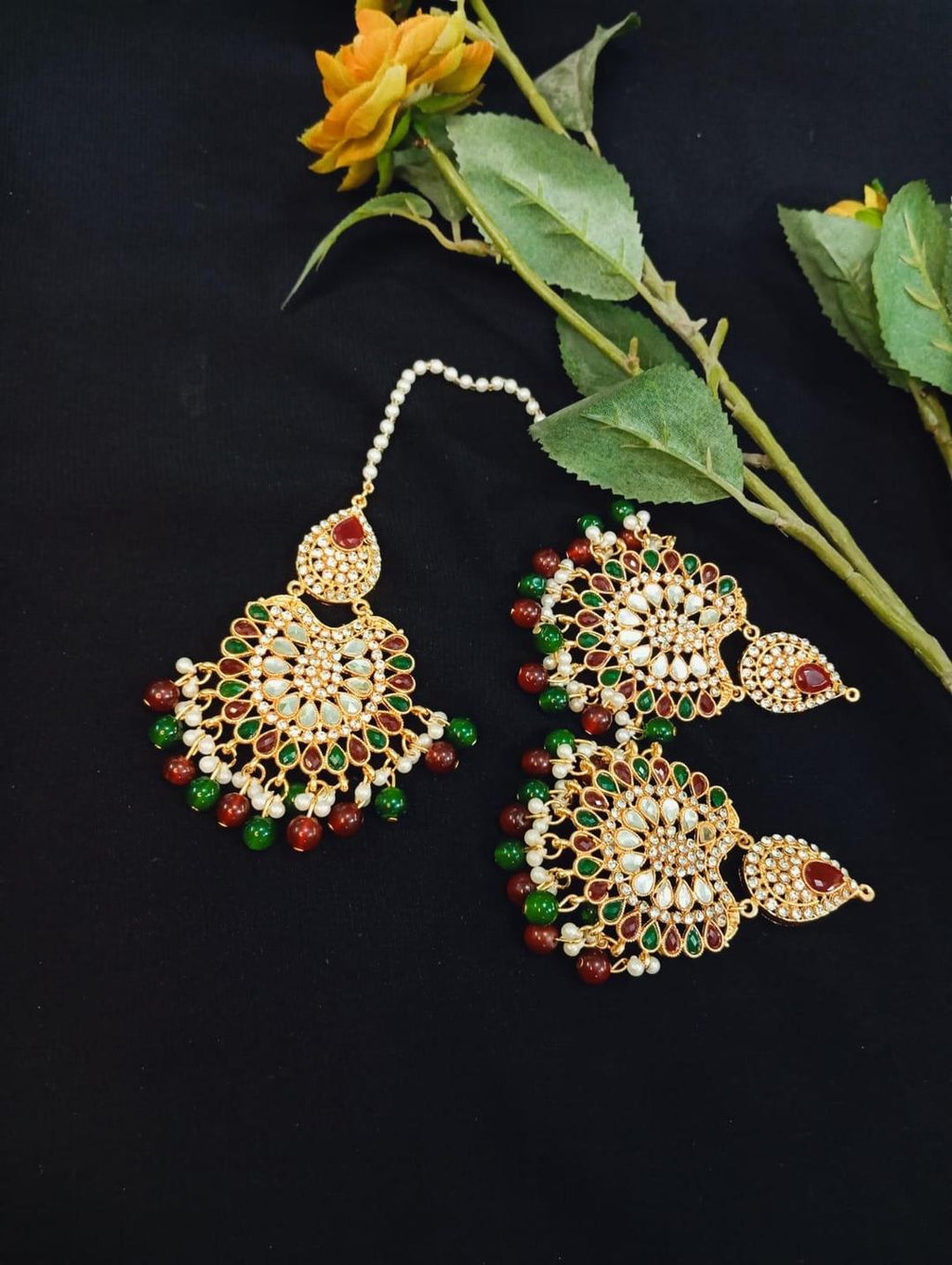 Ornate gold earrings with green and red stones on a black background