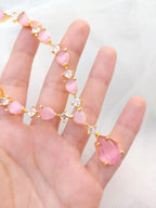Hand wearing a pink gemstone bracelet with gold accents on a white background