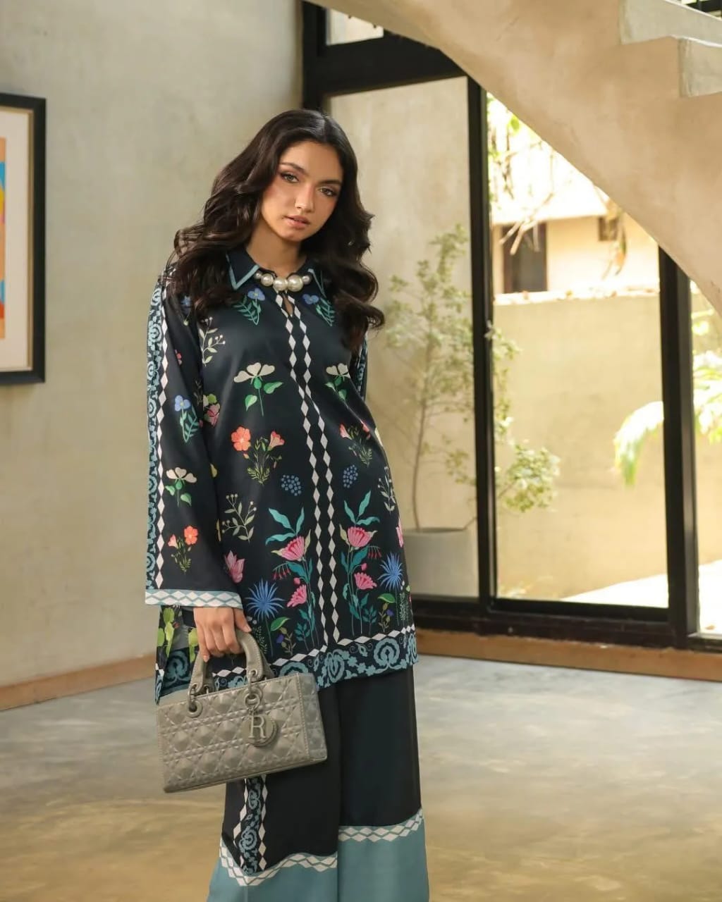 Woman wearing a floral embroidered outfit holding a handbag indoors.