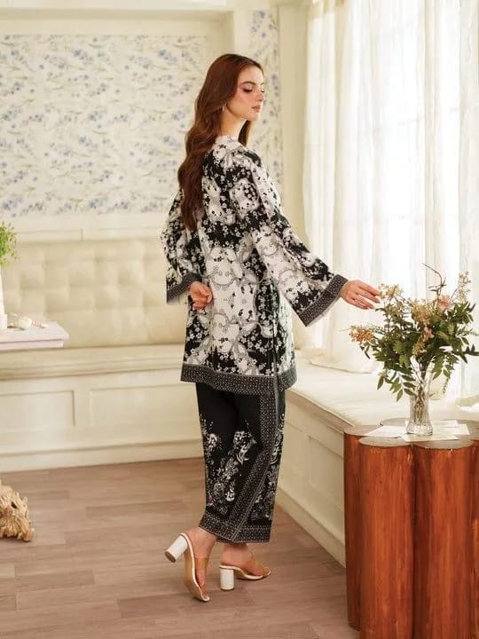 Woman in a black and white floral outfit standing in a room with floral wallpaper and a wooden table.