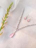 Jewelry set with pink teardrop pendant necklace and earrings on a light fabric background.