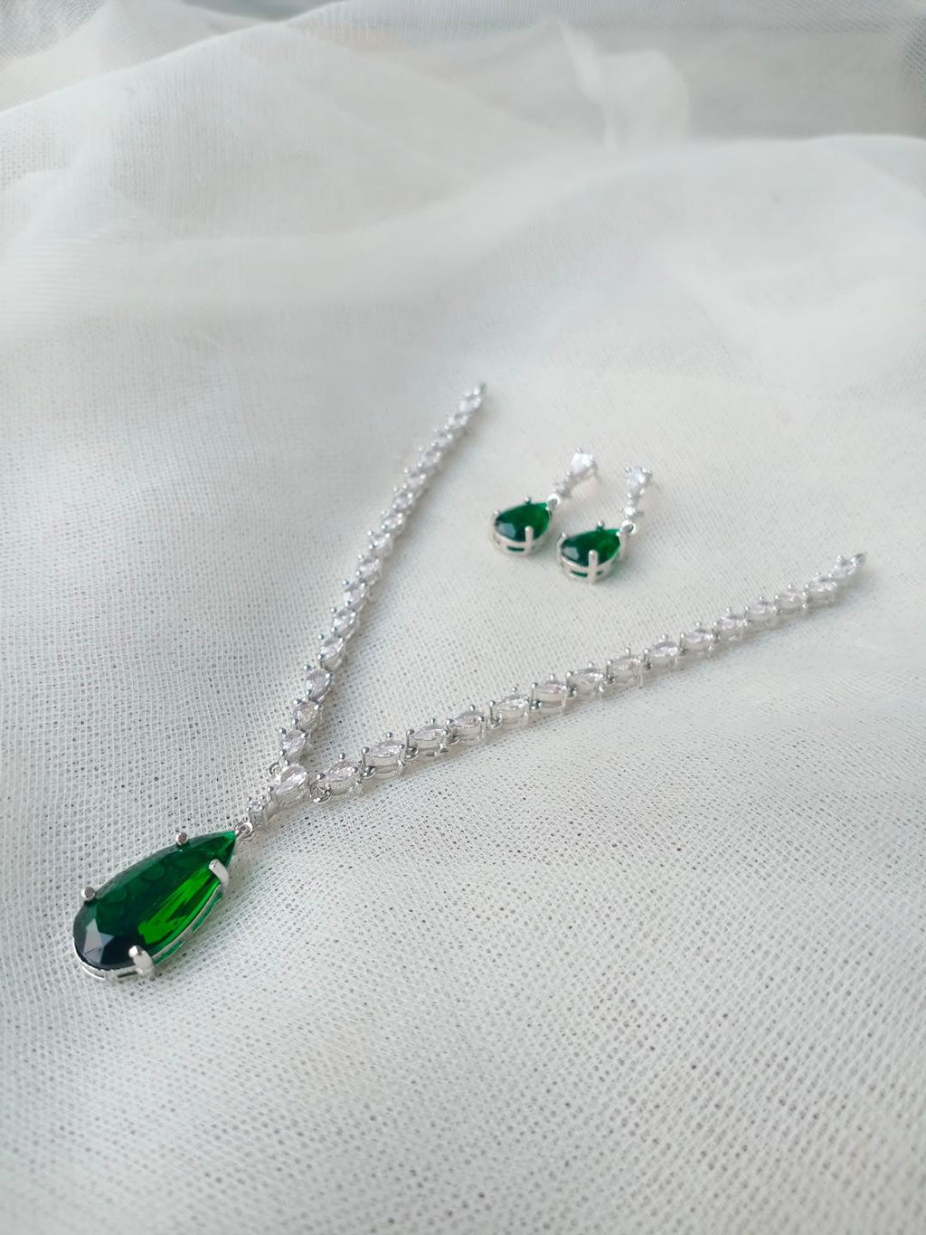 Jewelry set with green teardrop pendant necklace and earrings on a white fabric background