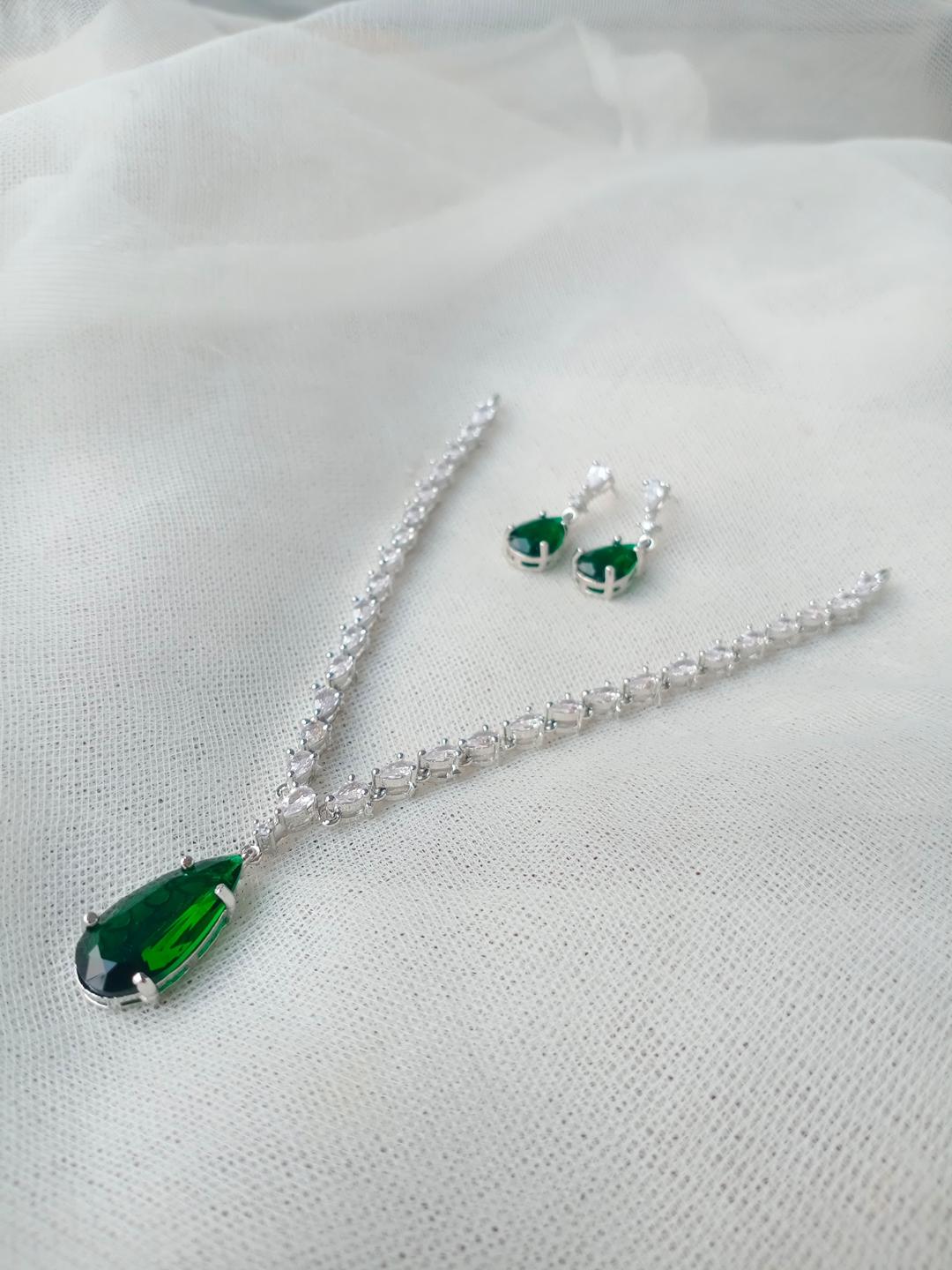 Jewelry set with green teardrop pendant necklace and earrings on a white fabric background
