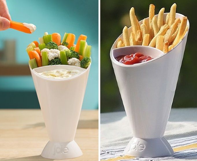 White cone-shaped containers holding vegetables and dip on one side, and fries with ketchup on the other, against a blurred background.