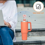 Person using a laptop with an orange mug featuring a pink bow on a stone surface.