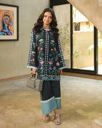 Woman in a black and blue embroidered outfit standing in a room with a colorful painting on the wall.
