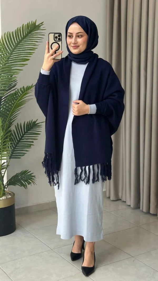 Woman taking a mirror selfie wearing a navy hijab and shawl over a white outfit, standing indoors.