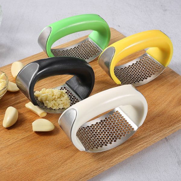 Four garlic press tools with different colored handles on a wooden board.